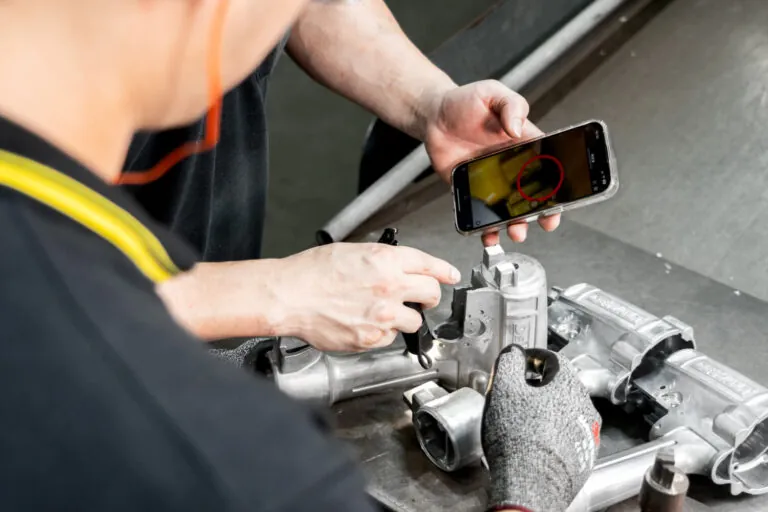 Production operator performing real-time process verification and visual inspection on aluminum pneumatic tool housings.